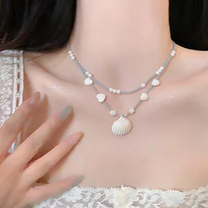 Detail view of a double-layered necklace featuring a natural shell pendant and pearls
