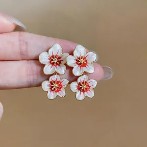 Sweet white floral enamel stud earrings with red accents and gold stamens held by hand