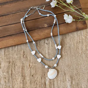 Detail view of double-layered beaded necklace with heart accents and a natural shell pendant