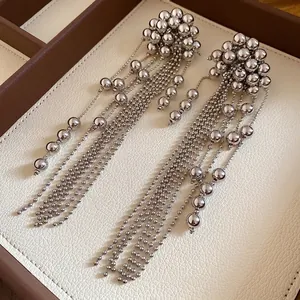Elegant minimalist silver-toned metallic ball tassel dangle earrings displayed on a textured tray