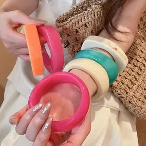 Detailed view of colorful geometric resin bracelets on a model's arm with straw bag