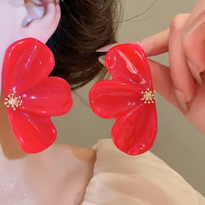 Close-up of vibrant red resin flower earrings worn by a model with golden pistil details