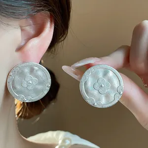Macro view of vintage matte silver stud earrings with intricate embossed floral patterns