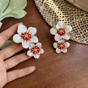 Macro view of sweet white and red enamel flower earrings with gold accents on wood