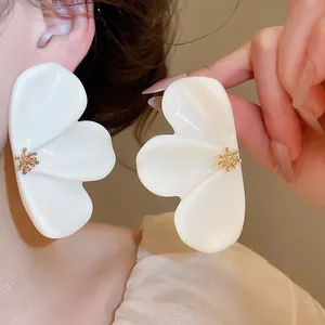 Detailed view of oversized white resin flower earrings featuring a textured gold stamen center.