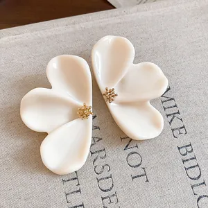 Macro detail of elegant cream resin flower earrings with gold textured pistil centers.