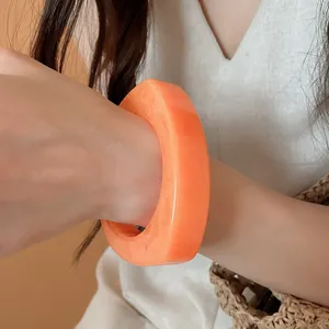 Close-up of large irregular orange resin bangle with marbled texture worn on wrist