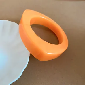 Close-up of a bold orange irregular geometric resin bangle leaning on a white dish
