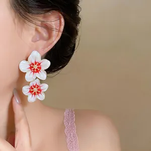 Detail shot of elegant white and red flower earrings worn by a model in soft light