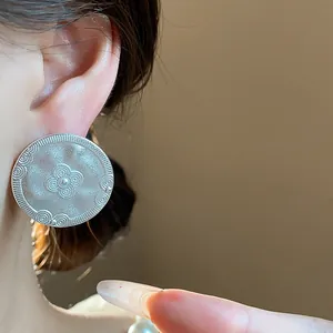 Close-up of matte silver round stud earrings with embossed floral patterns on ear