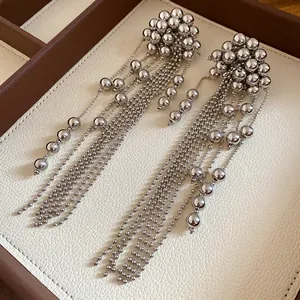 Close-up of silver-tone multi-strand bead tassel earrings on a textured tray.