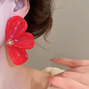 Close-up detail of large red resin flower earring with golden center on model