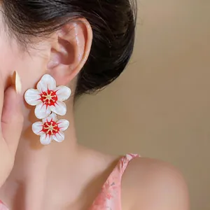 Close-up detail of sweet white and red enamel floral drop earrings worn on the ear
