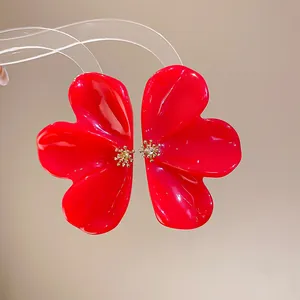 Close-up detail of glossy red resin flower earrings with intricate gold stamen accents