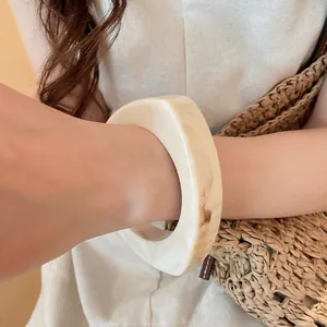 Close-up view of a cream marble-textured resin bangle with a geometric shape