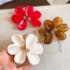Detail view of oversized resin flower earrings in stylish red, white, and amber colors.