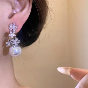 Detailed view of elegant silver floral earrings with white pearl drops worn on ear