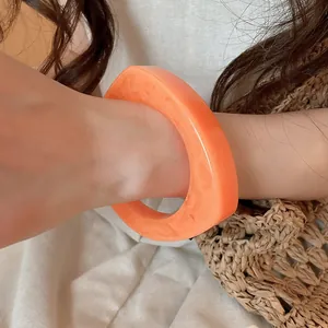Close-up view of an orange irregular geometric resin bangle worn on a female wrist.