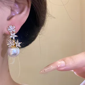 Elegant zircon flower and pearl drop earrings shown on a model's ear, close-up view details.