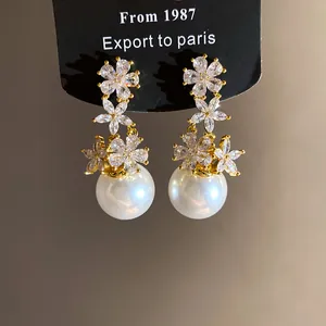 Detailed view of elegant flower zircon clusters and large white pearls on stud earrings.