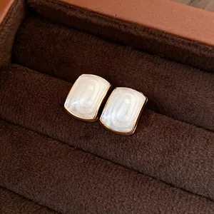 Détail rapproché d'élégantes boucles d'oreilles en résine crème avec cadre doré en boîte.
