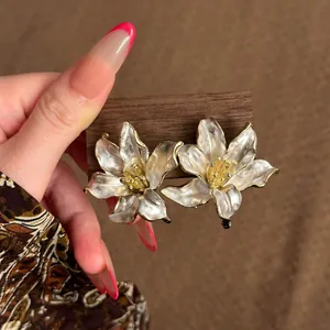 Primer plano detallado de elegantes pendientes de lirio en esmalte blanco y dorado.