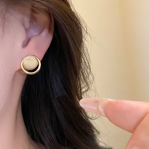 Élégantes boucles d'oreilles rondes en résine avec cadre doré sur une oreille