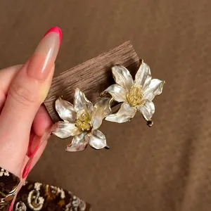 Vista detallada de pendientes de flores nacaradas con acabado dorado y esmalte