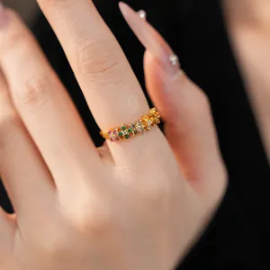 Close-up of a delicate gold ring with colorful zircon floral clusters on a finger
