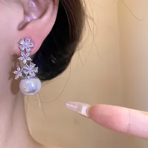 Detailed close-up of a floral zircon stud earring with a large white pearl drop.