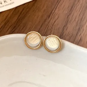Gros plan de boucles d'oreilles rondes en résine avec bordure dorée et tiges en argent pur