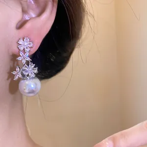 Detail view of zircon flower earrings with large pearl drop worn on ear