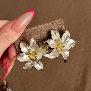 Primer plano de pendientes de flores elegantes con esmalte perlado y bordes dorados.