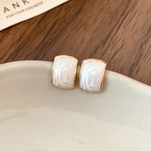 Gros plan d'élégantes boucles d'oreilles en résine blanche et bordure dorée sur céramique.