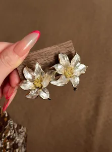 Detalle de elegantes pendientes de lirio en esmalte blanco con bordes dorados y agujas de plata.