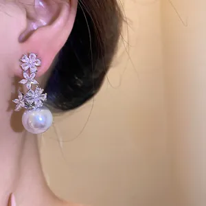 Detailed view of silver stud earrings with zircon flowers and a large white pearl drop.
