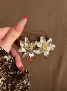 Vista detallada de elegantes pendientes de flor en esmalte blanco con bordes dorados.