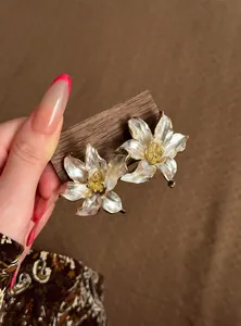 Primer plano de elegantes pendientes de flor crema con detalles dorados
