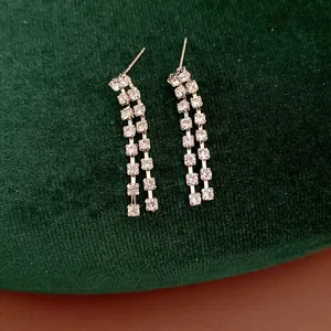 Dettaglio di orecchini a nappa con strass argento su sfondo di velluto verde scuro.