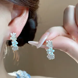 Dettaglio di orecchini a forma di C con fiori in smalto blu e zirconi indossati da modella
