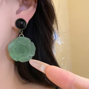 Detailed view of a green resin rose pendant earring worn on ear with black circular stud