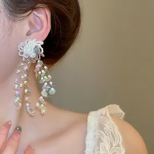 Detailed close-up of large white flower tassel earrings with iridescent sequins on model