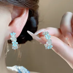 Primo piano di eleganti orecchini a C con fiori in smalto azzurro e zirconi brillanti.
