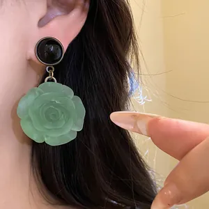 Close-up of elegant green resin rose pendant earring worn on ear, silver needle