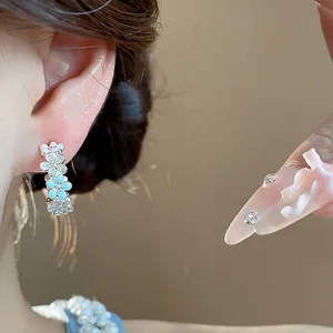 Primo piano di eleganti orecchini a fiore a forma di C con zirconi e smalto azzurro.
