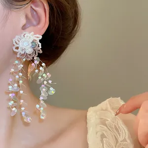 Close-up of handmade white flower earrings with iridescent sequin tassels worn on ear.