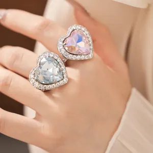 Close-up of two sparkling heart-shaped zircon rings in pink and blue on fingers.