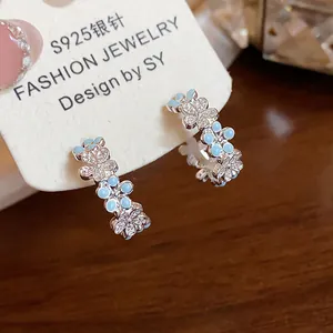 Dettaglio macro di orecchini a cerchio a C in argento con fiori in smalto blu e zirconi