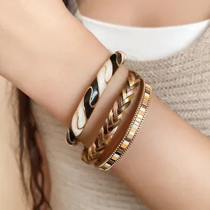 Close-up of Maillard style stacked enamel twisted bangle and braided metallic bracelet set.
