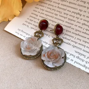 Close-up of vintage resin rose earrings with red studs on a printed book page background.